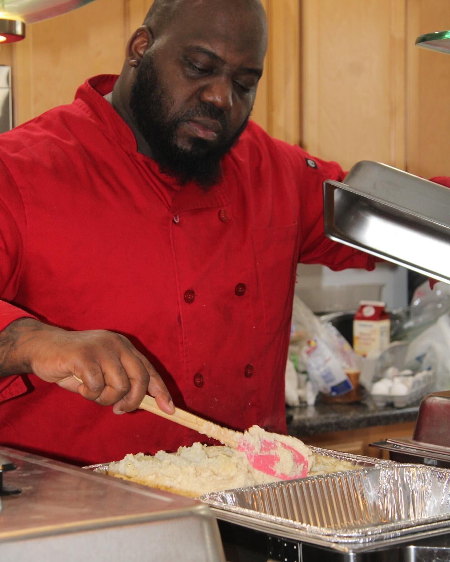 confident african american chef in red chef coat smiling at camera in professional kitchen setting